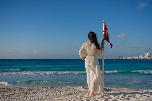 A woman stands on the beach near the red flag. Mexico.