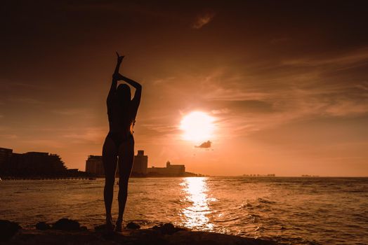 Slender blonde woman admires the sunrise at sea.