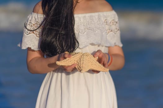 Woman in a white dress holds a starfish.