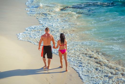 A man and a woman walk on the seashore.