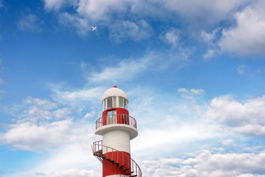 Top of a white-red lighthouse against a blue sky with an airplane. Mexico.