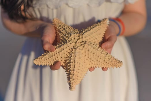 Woman in a white dress holds a starfish.