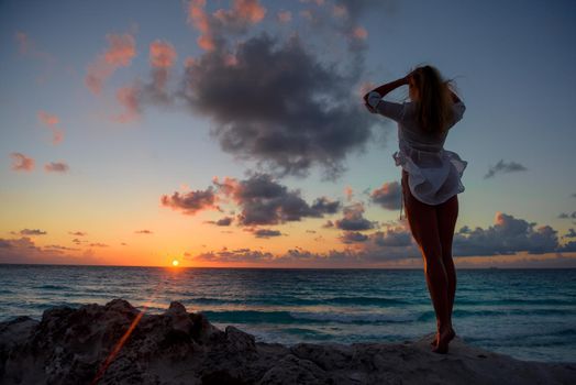 Slender blonde woman admires the sunrise at sea.