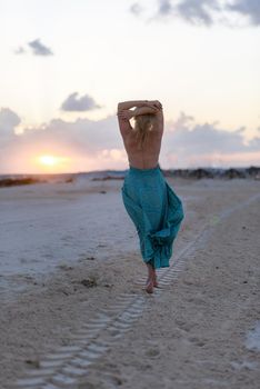 Slender blonde woman admires the sunrise at sea.