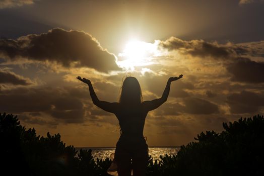 Slender blonde woman admires the sunrise at sea.