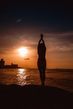 Slender blonde woman admires the sunrise at sea.