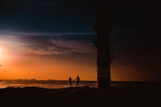 The silhouette of a couple and a huge lighthouse against the backdrop of the sea and the setting sun. Mexico.