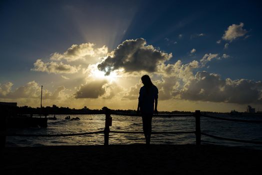 Slender blonde woman admires the sunrise at sea.