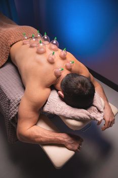 Vertical shot Relaxed young muscular man getting cupping treatment on his back lying on table.