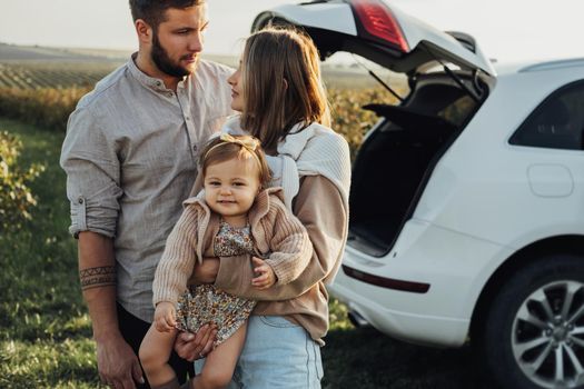 Young Caucasian Family Enjoying Road Trip, Mother and Father with Little Daughter Outdoors with SUV Car on Background