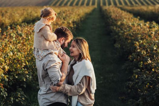 Happy Young Family Outdoors, Mother and Father with Their Baby Daughter at Sunset in Field