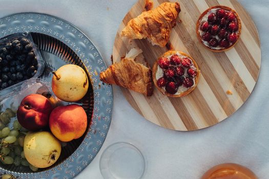 Flat Lay of Picnic Set, Fruits and Cakes with Croissants Laid Up on Plaid at Sunset