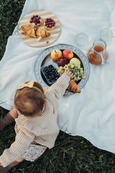 Vertical Flat Lay of Little Baby Girl on Picnic Outdoors, Fruits and Cakes with Croissants Laid Up on Plaid at Sunset