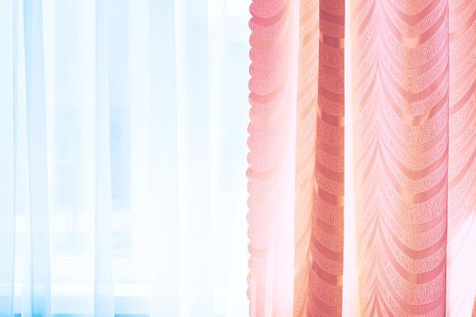 a piece of material suspended at the top to form a covering or screen, typically one of a pair at a window. Golden curtains and tulle on the window in the warm midday sun