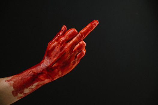 Female hand stained with blood shows the middle finger on a black background