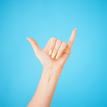 Studio shot of an unrecognisable woman showing a shaka hand sign against a blue background.