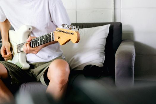Man playing electrical guitar on sofa at home