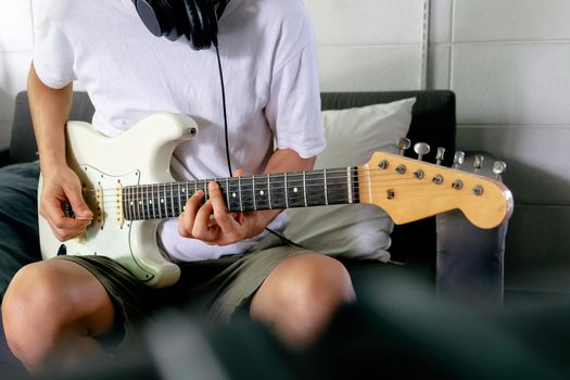 Man playing electrical guitar on sofa at home