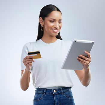 a woman holding a bank card and using a digital tablet against a grey background.