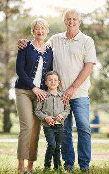 Portrait of loving caucasian grandparents enjoying time with grandson in nature. Smiling little boy bonding with grandmother and grandfather. Happy seniors and child standing together outdoors.