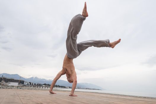 Shirtless caucasian man doing backflip on pebble beach