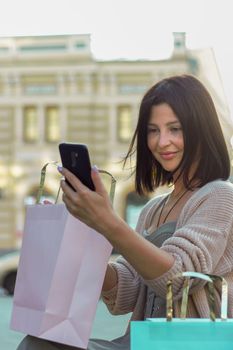 Young beautiful shopper woman smiling happy going to the shops sales holding shopping bags ourtdoors, smiling happy using smartphone