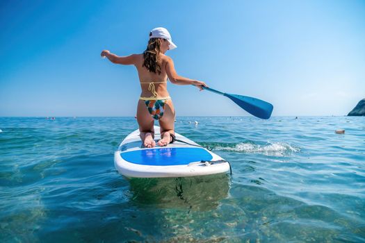 young woman in swimsuits doing yoga on sup board in calm sea, early morning. Balanced pose - concept of healthy life and natural balance between body and mental development