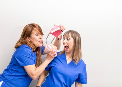 Portrait of two dentist women being silly and playing with a sample denture after a day of work at the dental clinic hall