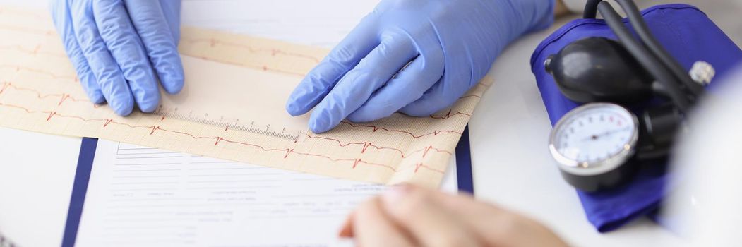 Close-up of professional cardiologist doctor examine electrogram scheme in clinic. Patient wait for result and prescription. Cardiology, checkup concept