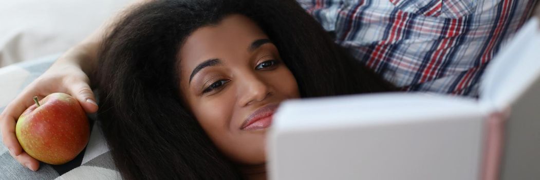 Portrait of latino american young woman reading interesting book laying on fathers lap. Smiling female get new knowledge, spare time at home. Hobby concept