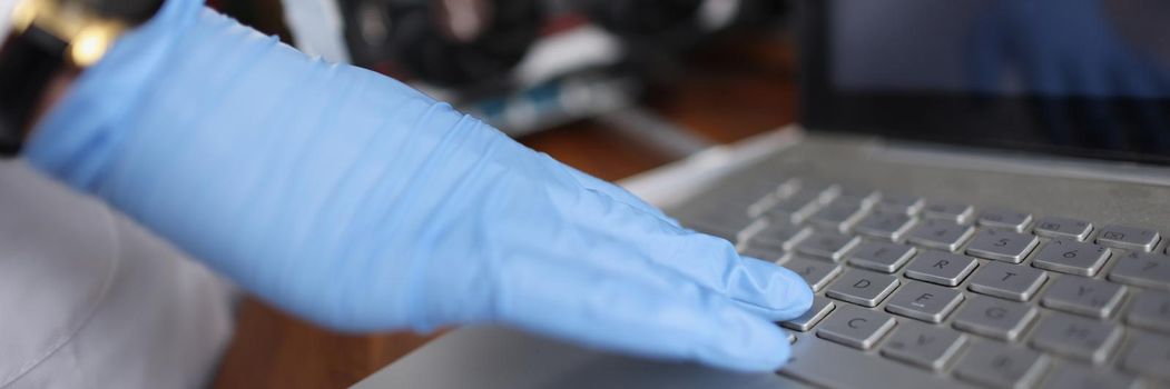 Close-up of professional technician man touching laptop keyboard wearing sterile gloves. Person check device on hidden failure. Tech maintenance concept