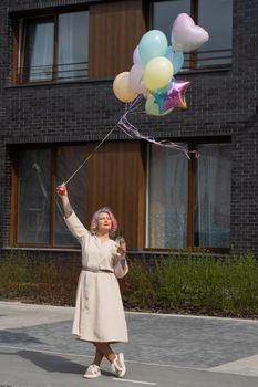 Woman in colored hair walks with an armful of balloons and drinks a refreshing beverage.