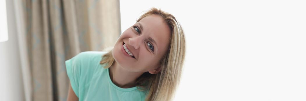 Portrait of happy smiling blonde young woman in apartment posing on curtain. Cheerful full of joy female at home. Modeling, relaxation, housewife concept