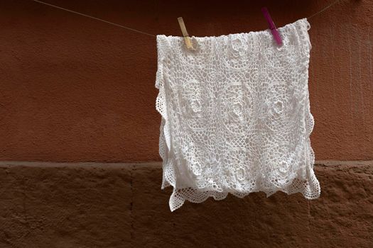 White crochet tablecloth, hung on the wire for hanging, to dry after washing. Background with brown wall.