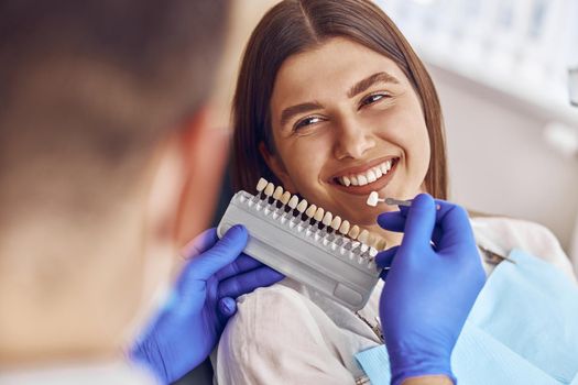 Professional doctor is choosing a colour of teeth in modern dental clinic