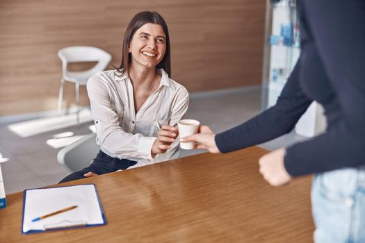 Happy woman is taking a paper cup from receptionist in modern dental clinic