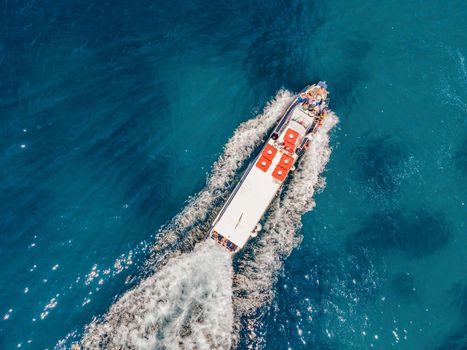 Ferry boat with tourists on the move on floats on turquoise water. Drone view.