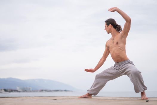 Caucasian man with naked torso practicing wushu on the seashore