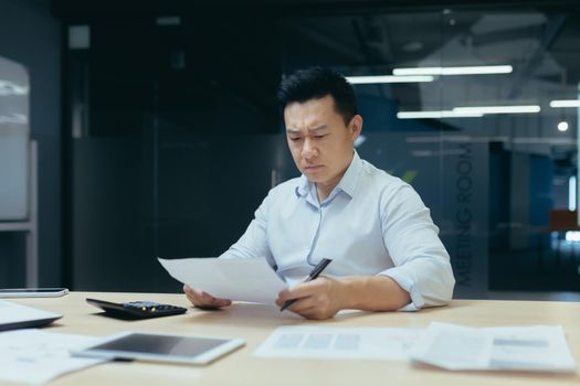 Upset and unhappy asian businessman reading documents and letter from bank, businessman at work in office disappointed with work result
