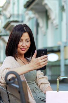 Young beautiful shopper woman smiling happy going to the shops sales holding shopping bags ourtdoors, smiling happy using smartphone