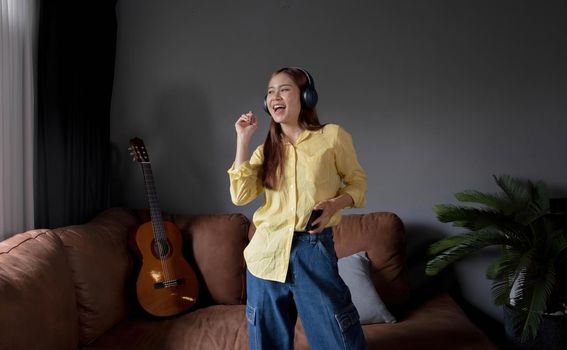 Young asian woman listening to music on couch in living room at home. Happy asia female using mobile smartphone, wearing headset