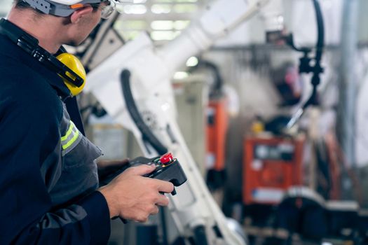 Young factory worker working with adept robotic arm in a workshop . Industry robot programming software for automated manufacturing technology .