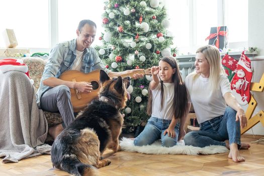 Excited girl and her family sitting on the floor near christmas tree and smiling. family during Christmastime.