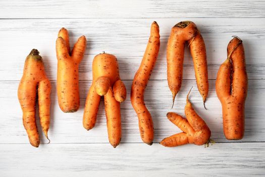 Several ripe orange ugly carrots lie on a light wooden surface. Selective focus.