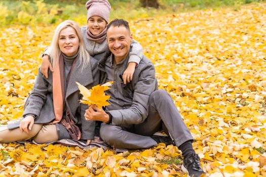 family, childhood, season and people concept - happy family playing with autumn leaves in park.