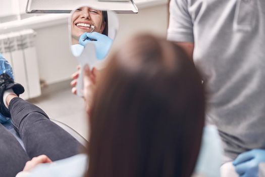 Happy woman patient is looking in mirror on her teeth and smiling