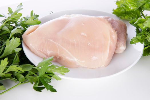 Raw chicken breast on a white plate surounded by parsley