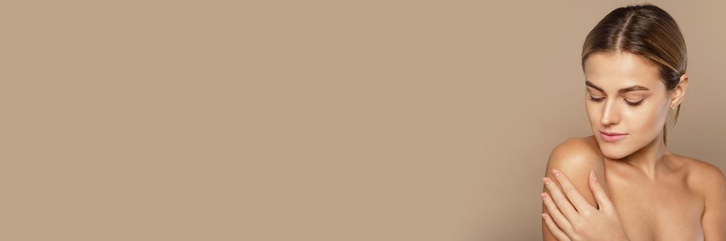Young lovely woman is touching her shoulder. Beautiful face of young woman with clean fresh skin on beige background. Copy space. Web banner