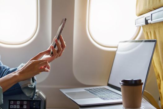 Attractive Asian woman sitting at window seat in economy class using mobile phone during inflight, travel concept, vacation, relax.