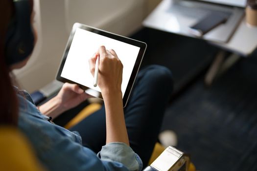 An Asian woman sits in a window seat in Economy Class using a white screen tablet that can use text or advertising while flying. Travel, vacation, vacation ideas.